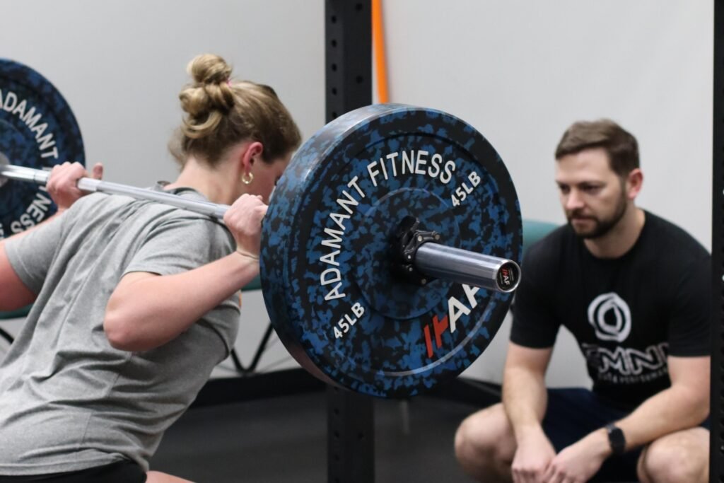 Physical therapist coaching female athlete during barbell squat training at Omni Wellness and Performance in Fairfax Virginia
